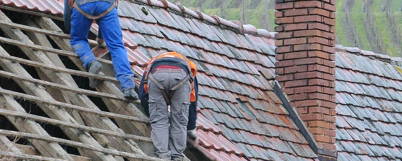 two person putting roof tiles on roof at daytime